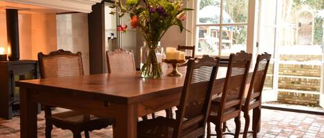 A dining area with a wooden table and chairs, a vase with flowers, and a view of the outside through large windows.