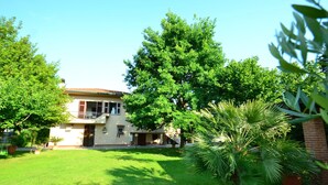 A two-story house with a balcony, surrounded by lush green trees and a well-maintained lawn. - Belvilla by OYO Serena (Massa)