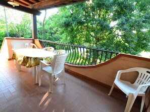 A covered patio with a table and chairs, a railing, and a view of greenery.