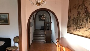 A hallway with a wooden staircase, a chandelier, and a large painting on the wall. - Belvilla by OYO Serena (Massa)