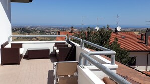 A balcony with wicker furniture, a metal railing, and a view of a town and sea. - A Serene Stay in Gemmano (Gemmano)