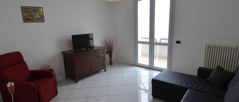 A living room with a TV on a wooden cabinet, a red chair, a black sofa, and a pendant light.