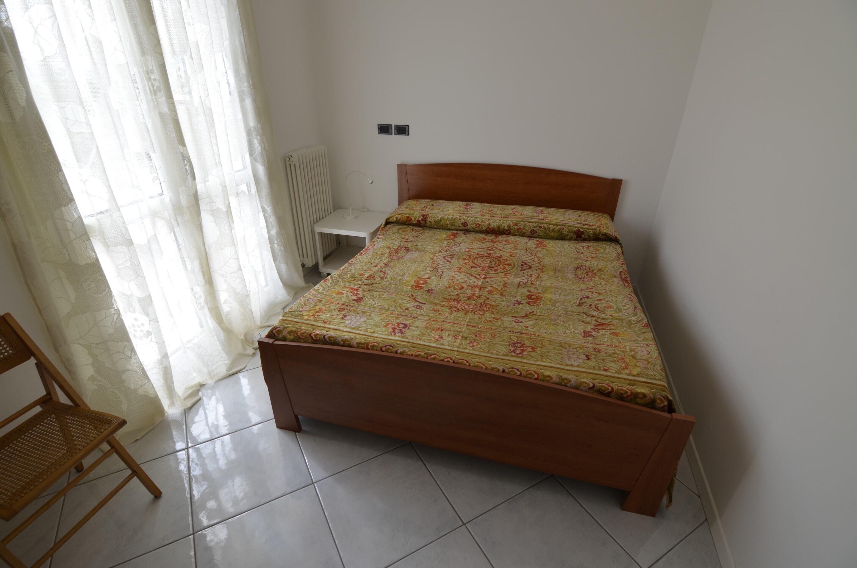 Een compacte, verzorgde slaapkamer met een houten bed, een stoel en een radiator.
