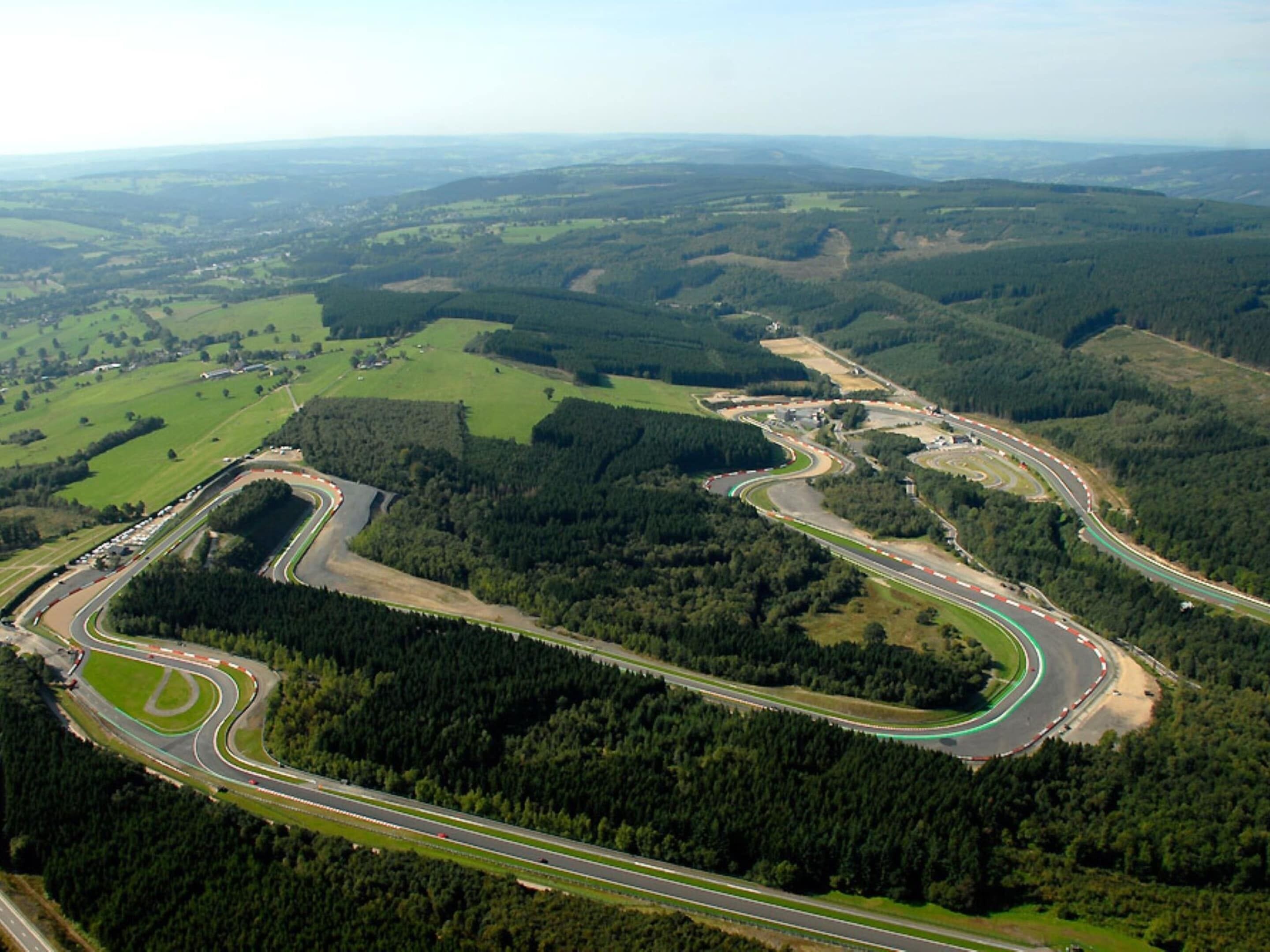An aerial view of a winding race track surrounded by dense forests and open fields.
