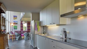 Una cocina moderna con armarios grises, un refrigerador de acero inoxidable y un horno empotrado. Hay un comedor con mesa y sillas, y una escalera que lleva a un nivel superior.