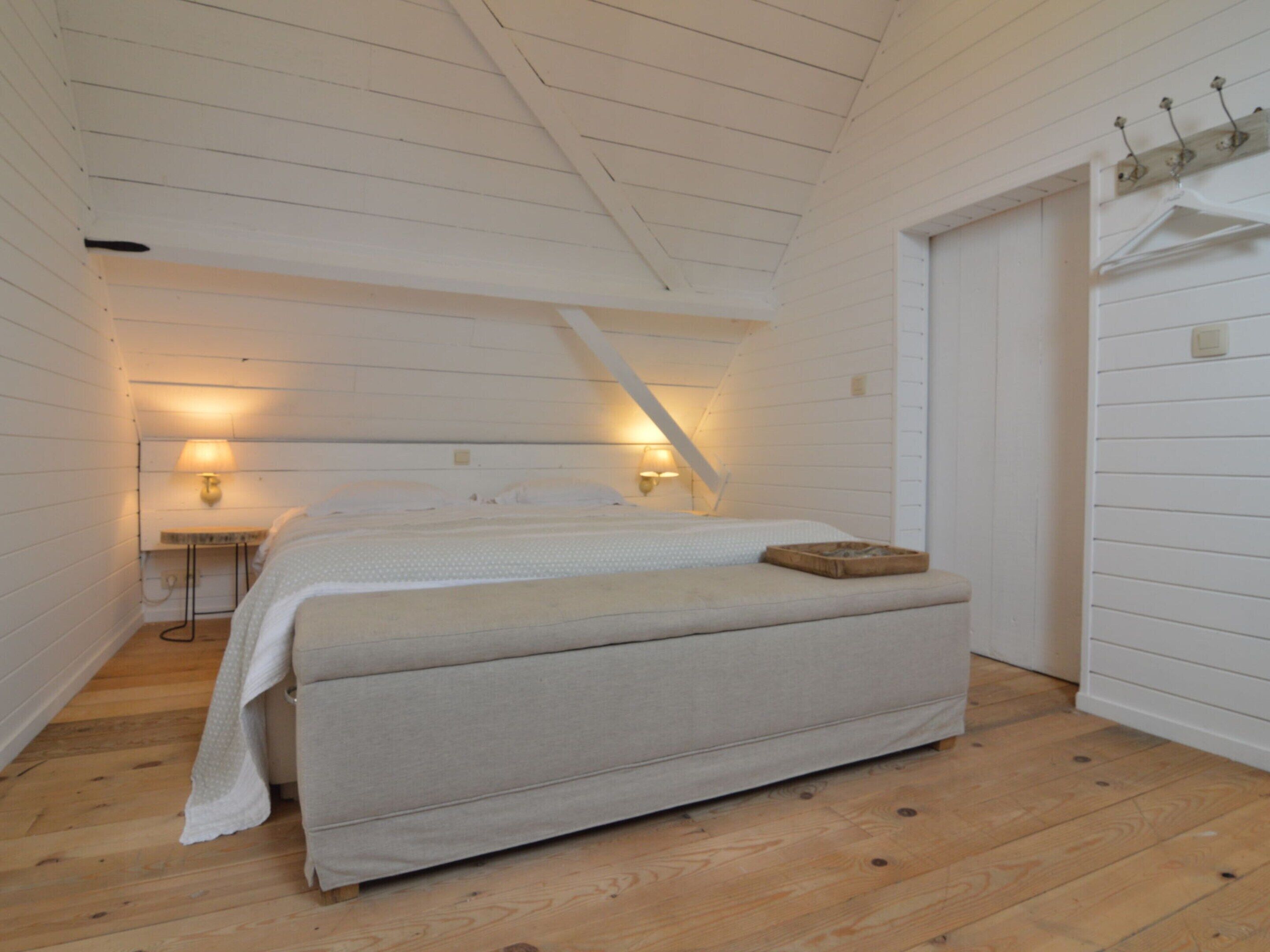Un dormitorio con cama, lámparas de noche, suelo de madera y techo inclinado.
