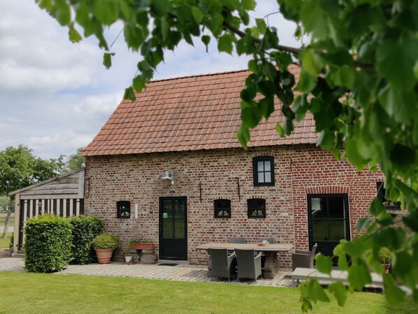 A brick building with a tiled roof, a front door, and a small outdoor seating area with a table and chairs.