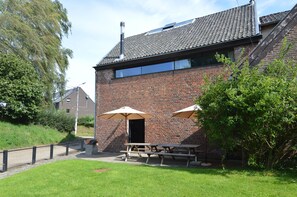 A brick building with a tiled roof, a picnic table with umbrellas, and a grassy area.