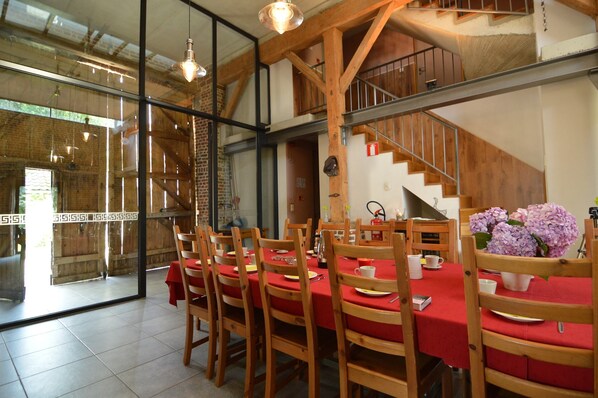A dining area with a long table, wooden chairs, and a staircase in the background.