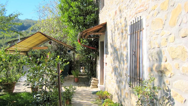 A stone building with a covered patio, potted plants, and a pathway leading to a door. - Cottage in Marliana With Private Pool (Marliana)