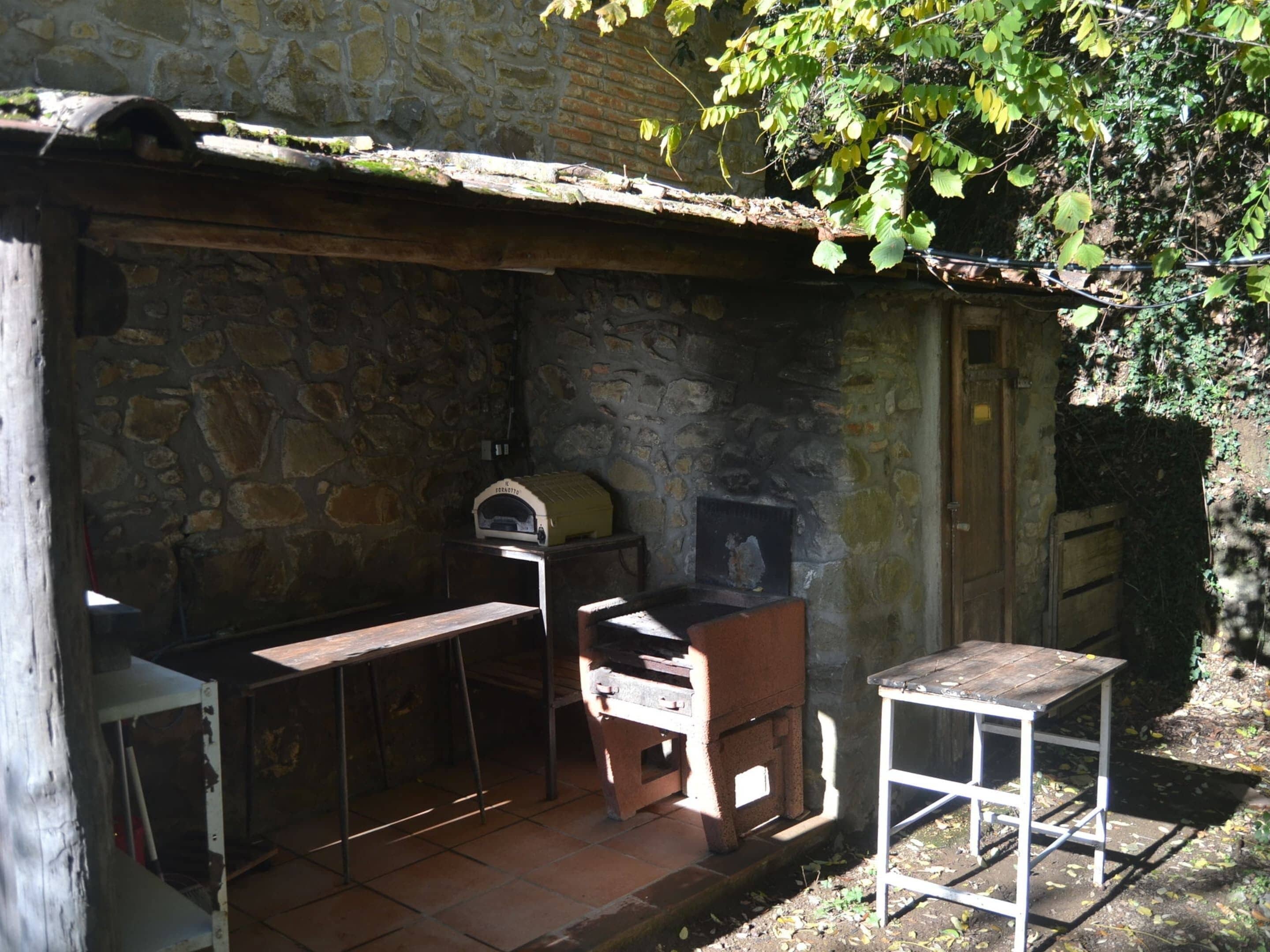 Ein Steinhaus mit einem rustikalen Außenbereich und einer Küche, darunter ein Holzofen und ein Tisch.