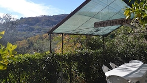 A covered outdoor seating area with a 'Happy Holiday' sign, surrounded by lush greenery and a view of a hilly landscape. - Cottage in Marliana With Private Pool (Marliana)