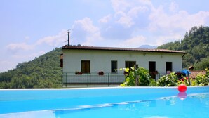 A swimming pool with a view of a white building with a red roof, surrounded by greenery and hills.