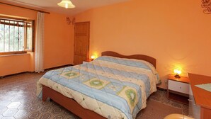 A bedroom with a bed, a nightstand, a desk, a window with curtains, and a door.