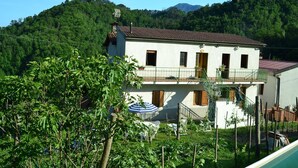 A two-story building with a balcony, surrounded by greenery and mountains.