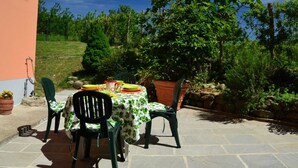 An outdoor patio with a table set for two, surrounded by greenery and a stone wall.