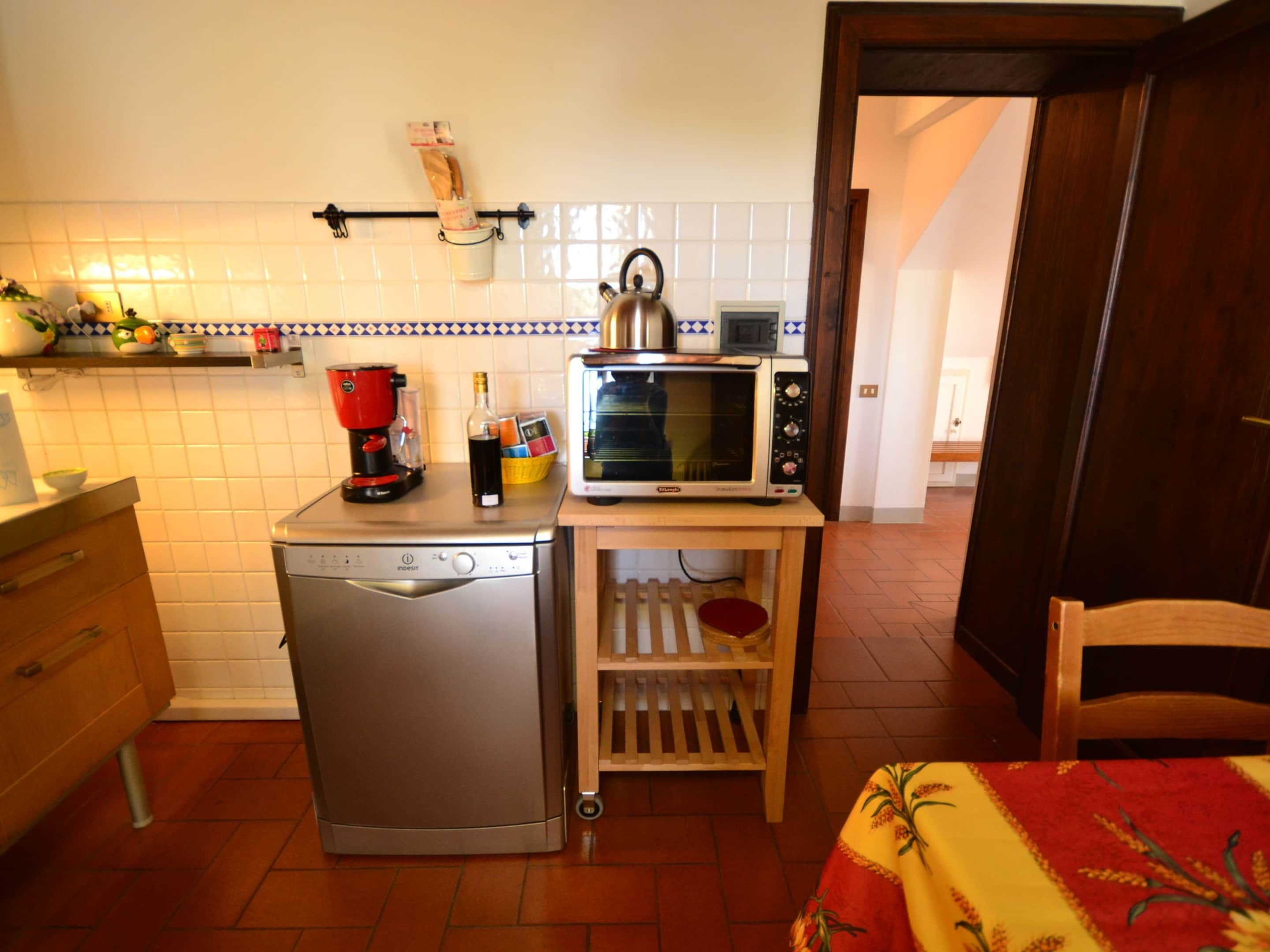 Una cocina compacta con lavavajillas, cafetera, microondas y un pequeño estante de madera.