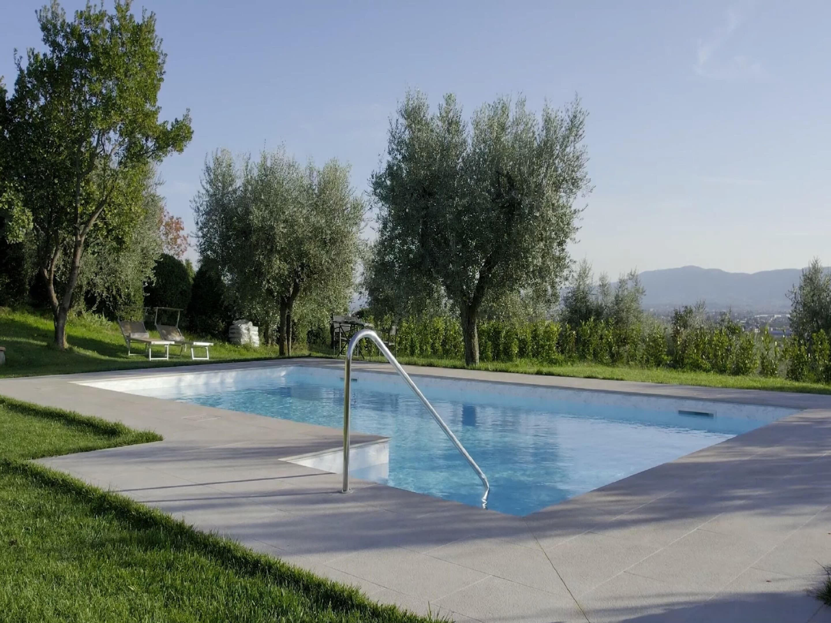 Ein rechteckiger Pool mit einer Metallleiter, umgeben von einer gepflasterten Terrasse und Rasen.