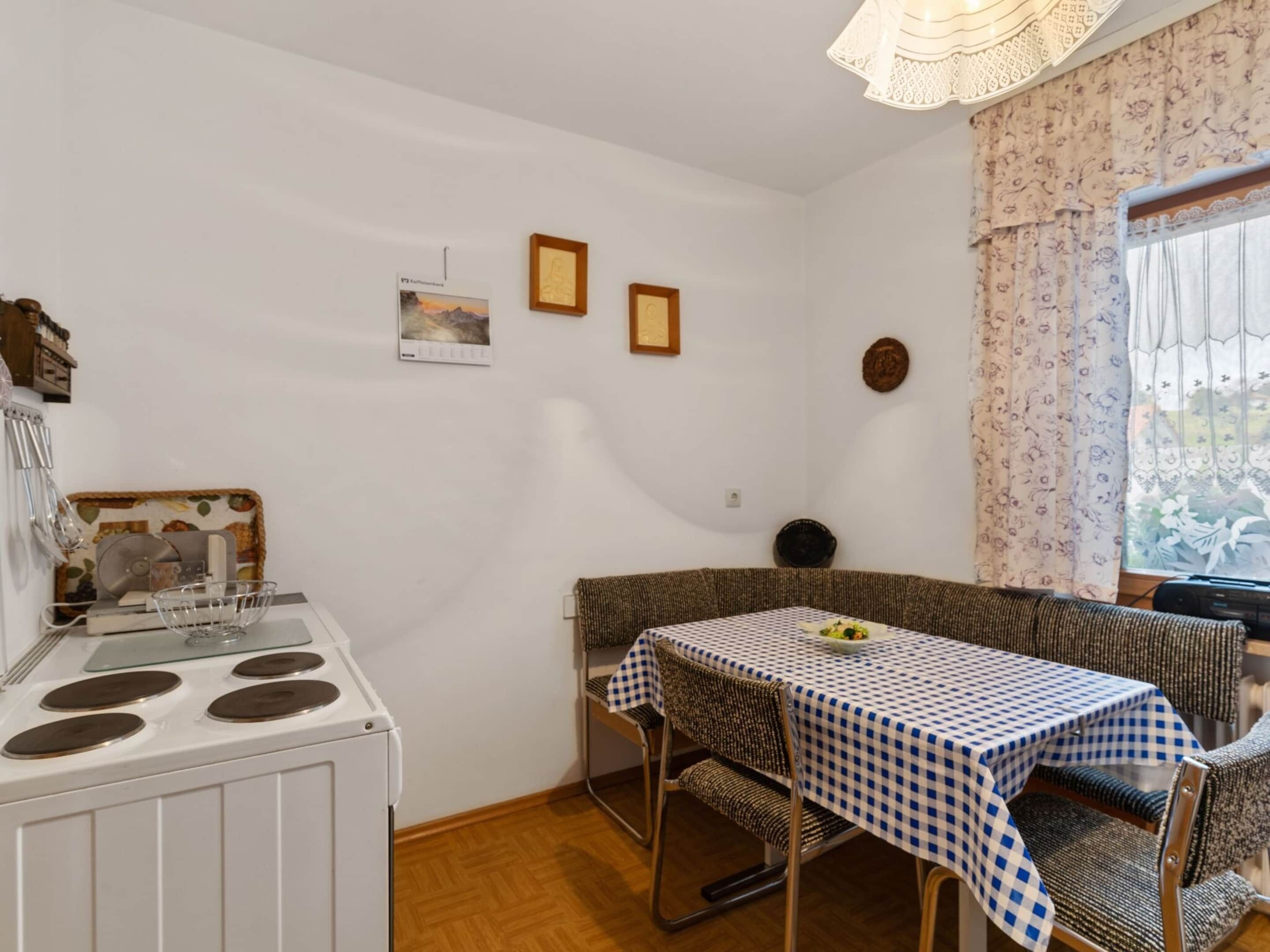 A compact kitchen with a stove, a dining table with a checkered tablecloth, and a bench.