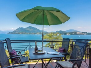 A terrace with a table, chairs, and an umbrella overlooking a body of water and mountains. - Holiday Home by Lake Maggiore With Pool (Stresa)