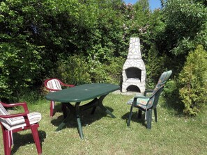 A stone outdoor oven, a green table, and two chairs in a garden.