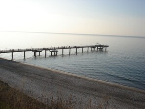 A pier extending into calm waters with a pebbled beach in the foreground.