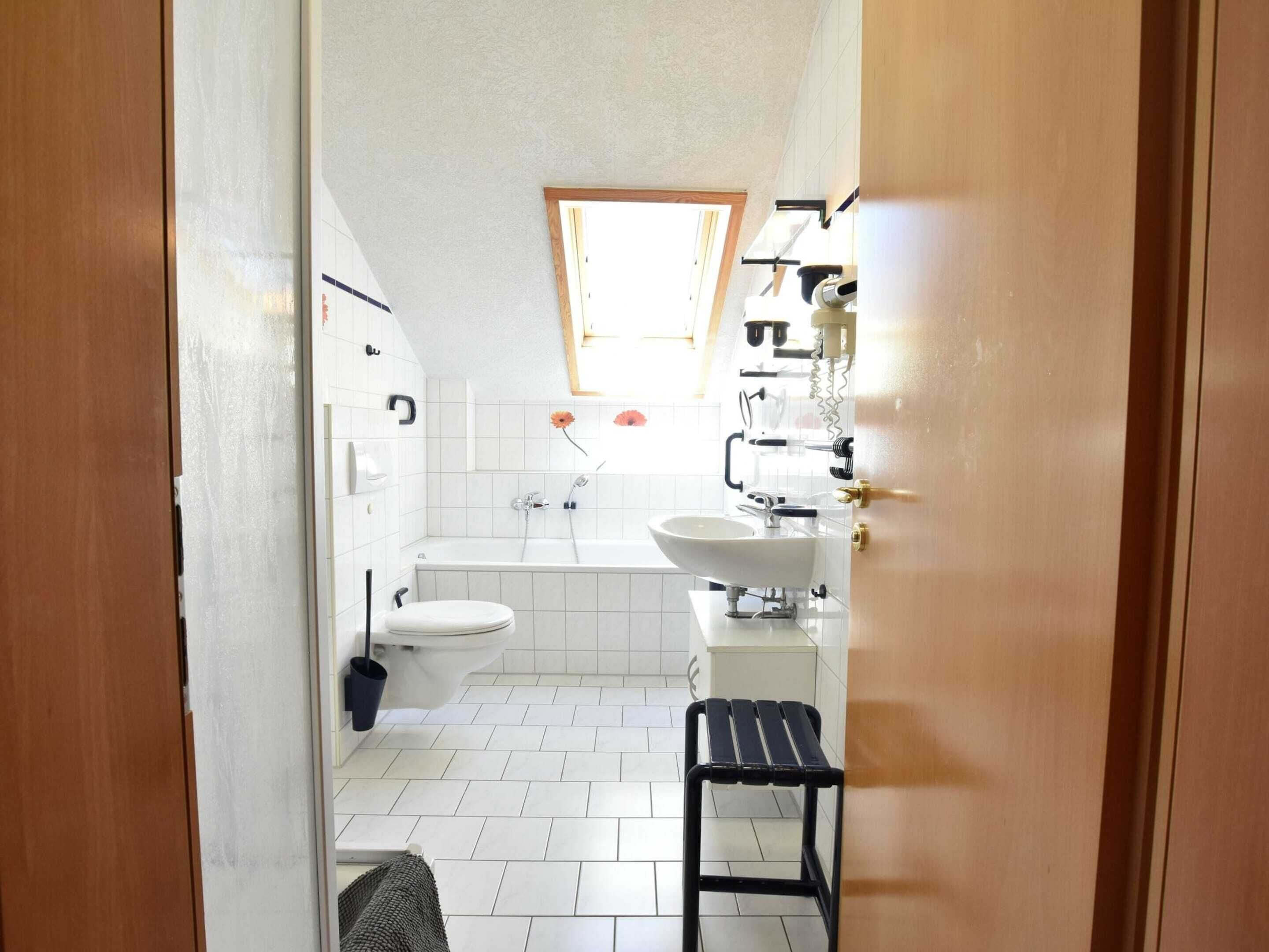 A small, compact bathroom with a toilet, sink, and bathtub. There is a window providing natural light and a towel rack.
