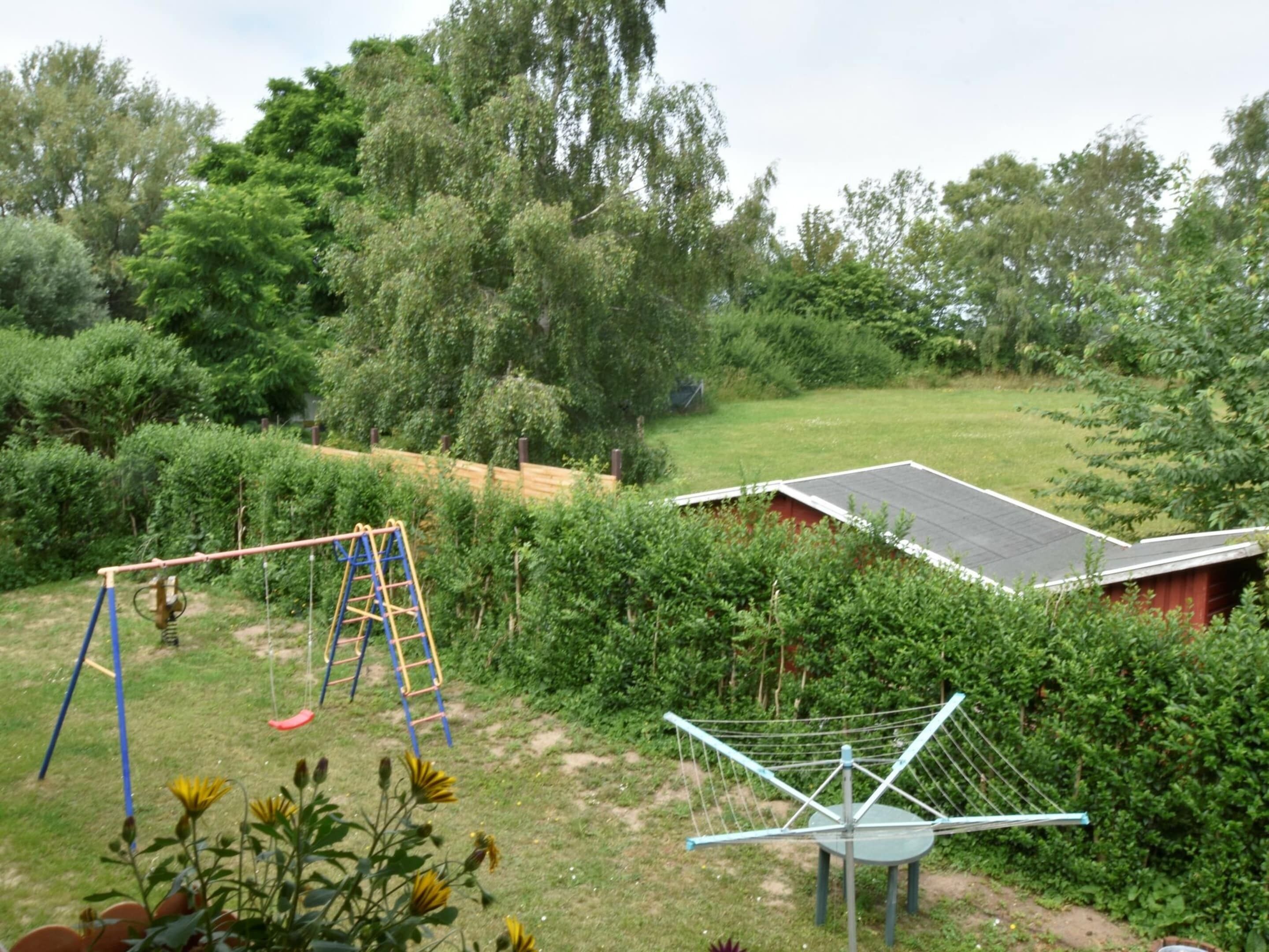 A garden with a swing set, a climbing frame, and a small shed.