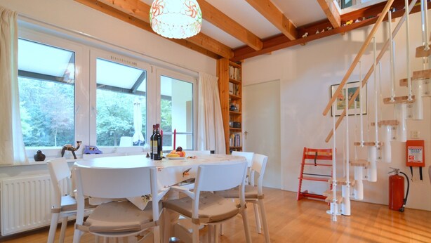 A dining area with a round table, white chairs, and a wooden ceiling. - Family Residence With Large Garden (Heino)