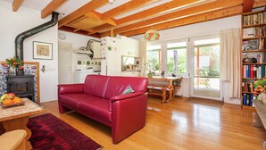 A cozy living room with a red leather sofa, wooden floors, a fireplace, and a kitchen in the background. - Family Residence With Large Garden (Heino)