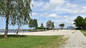 A park with a sandy area, a playground, and a building with a blue roof. - Charming Apartment in Langweer With Jetty (Langweer)