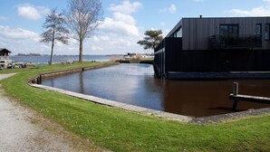 A modern building with a water feature in front, a grassy area, and a clear sky. - Charming Apartment in Langweer With Jetty (Langweer)