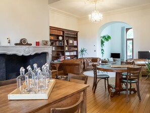 Un vaste salon doté d’une cheminée, d’une grande bibliothèque, de canapés en cuir, d’une table à manger avec des chaises et d’un lustre.