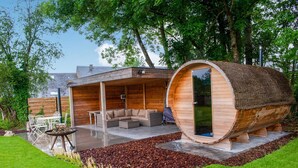 A modern log cabin with a large wooden barrel-shaped structure, a patio with outdoor furniture, and a well-maintained garden. - Beautiful Villa With Sauna in Chiny (Chiny)