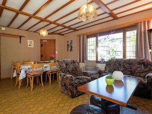 A dining area with a wooden table and chairs, a sofa, and a window with curtains. - Spacious Holiday Home With Large Garden (Amel)