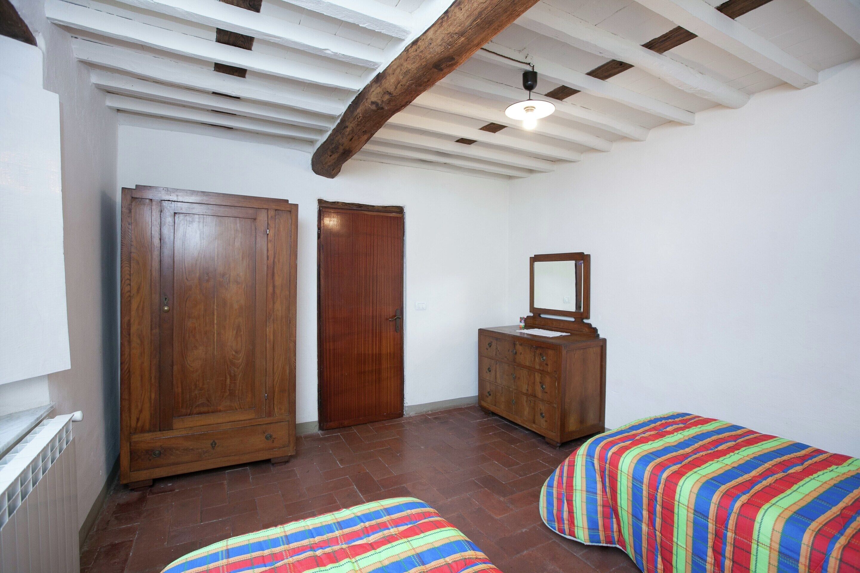A room with a wooden wardrobe, a cabinet with a mirror, and two beds with colorful bedding.