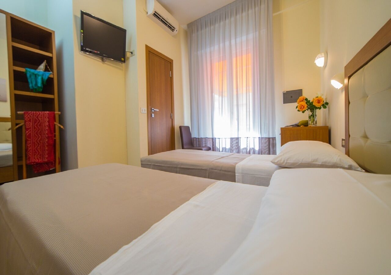Habitación de hotel con dos camas, televisor, armario y ventana con cortinas.