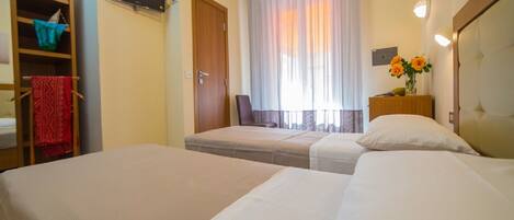 Habitación de hotel con dos camas, televisor, armario y ventana con cortinas.