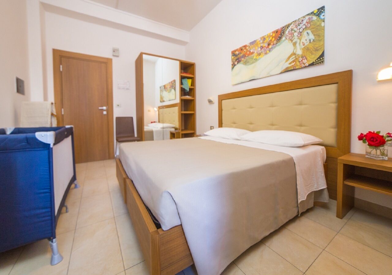 A hotel room with a bed, a desk, a chair, a wardrobe, and a painting on the wall.