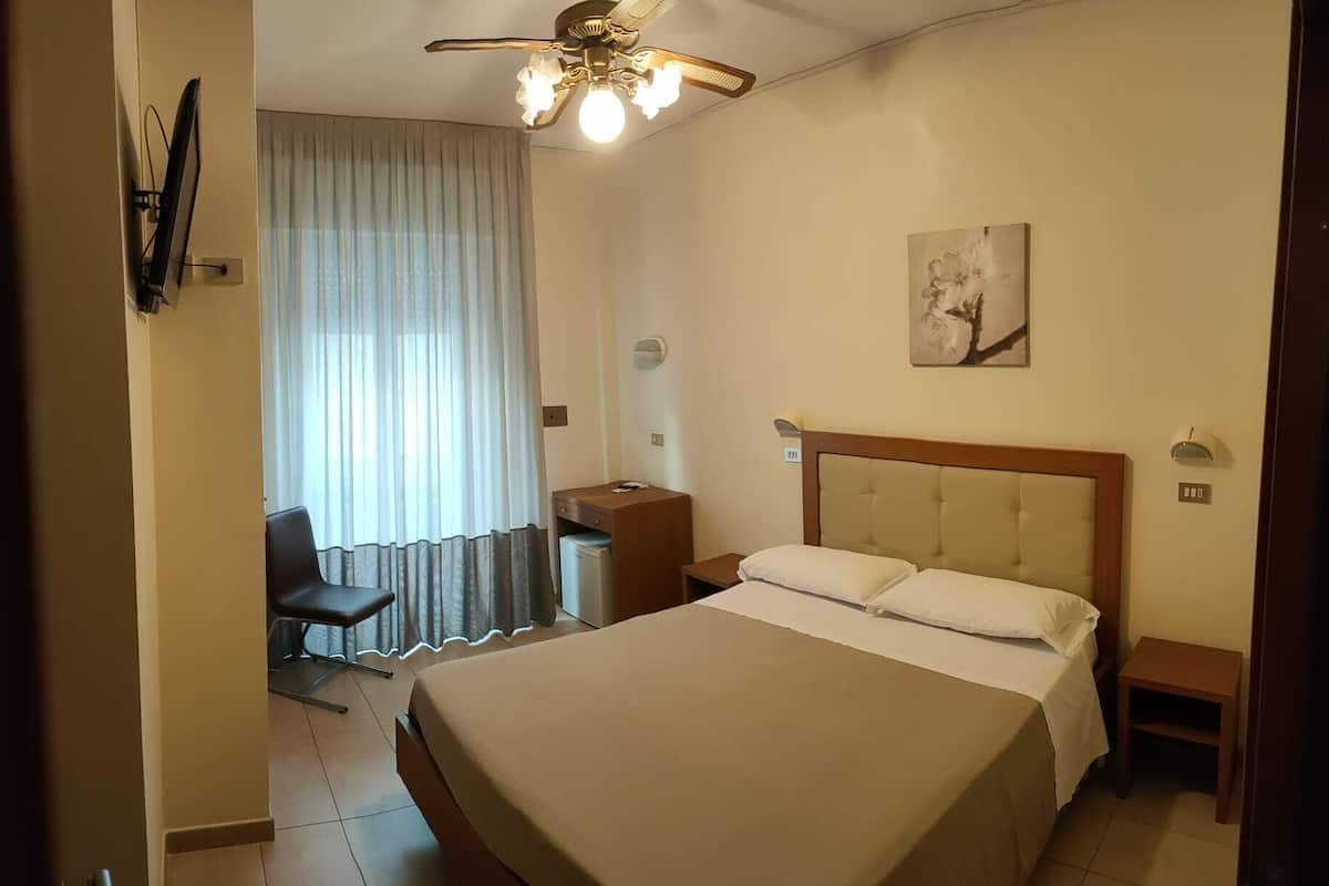 Een hotelkamer met een bed, een bureau, een stoel, een plafondventilator en een schilderij aan de muur.
