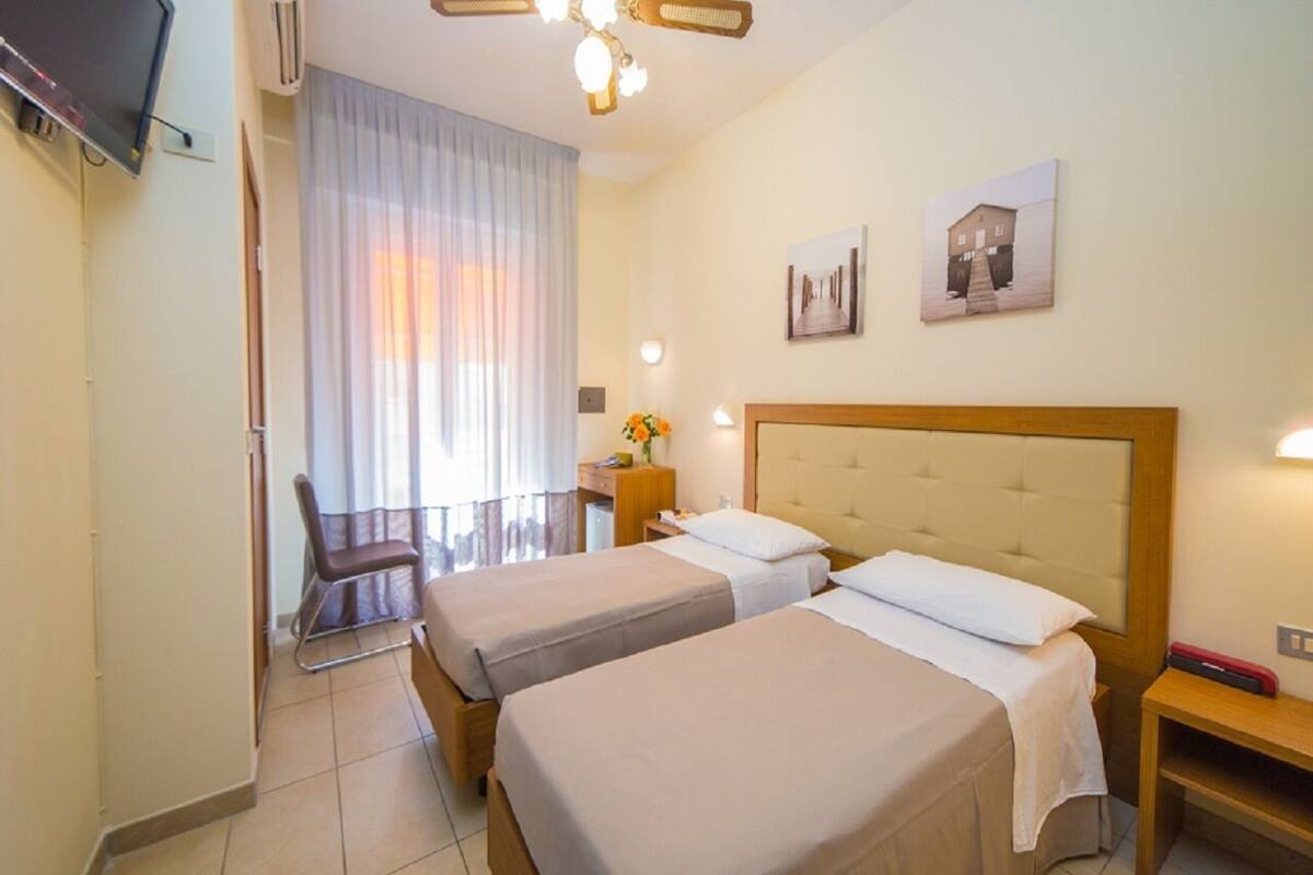 Een hotelkamer met twee bedden, een bureau, een stoel, een televisie en een raam met gordijnen.