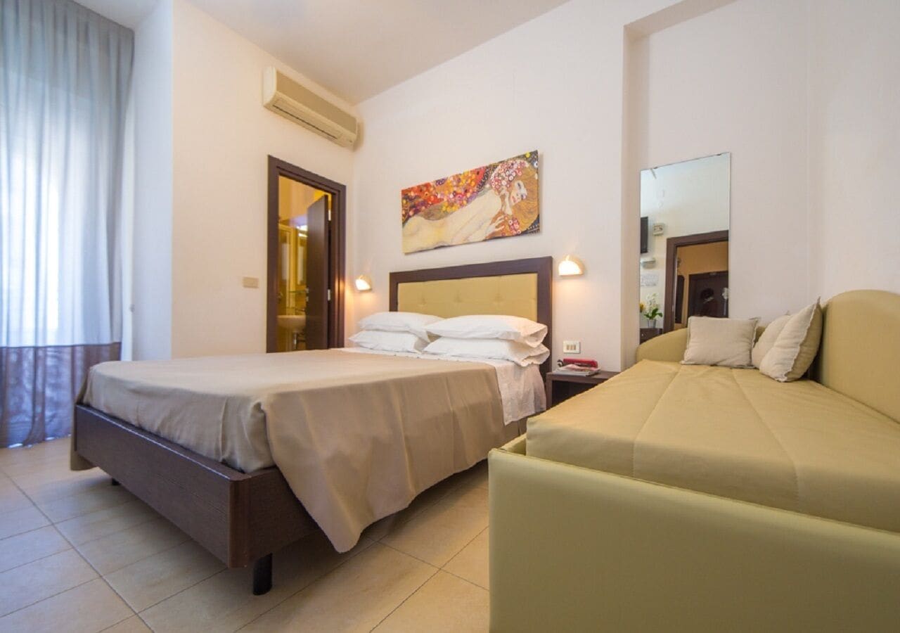 A hotel room with a bed, a sofa, and a painting on the wall.