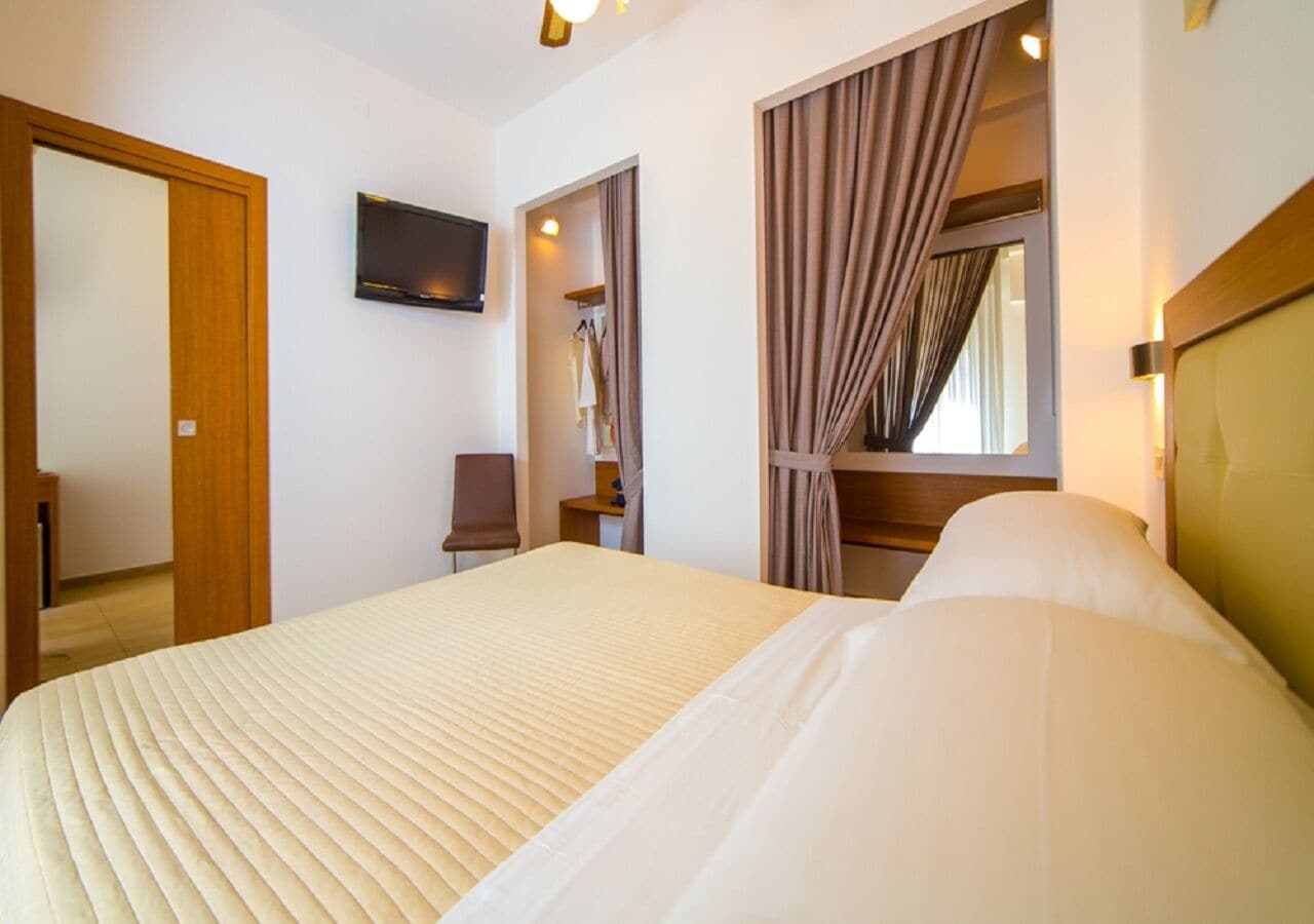 A hotel room with a large bed, a television mounted on the wall, and a wardrobe with a mirror.