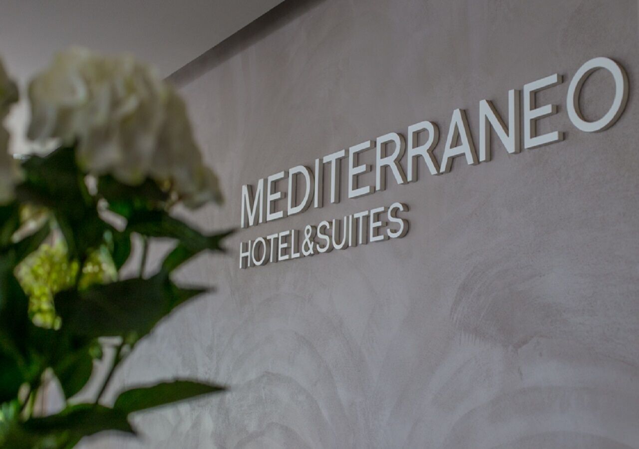 A sign for Mediterraneo Hotel & Suites with a floral design.
