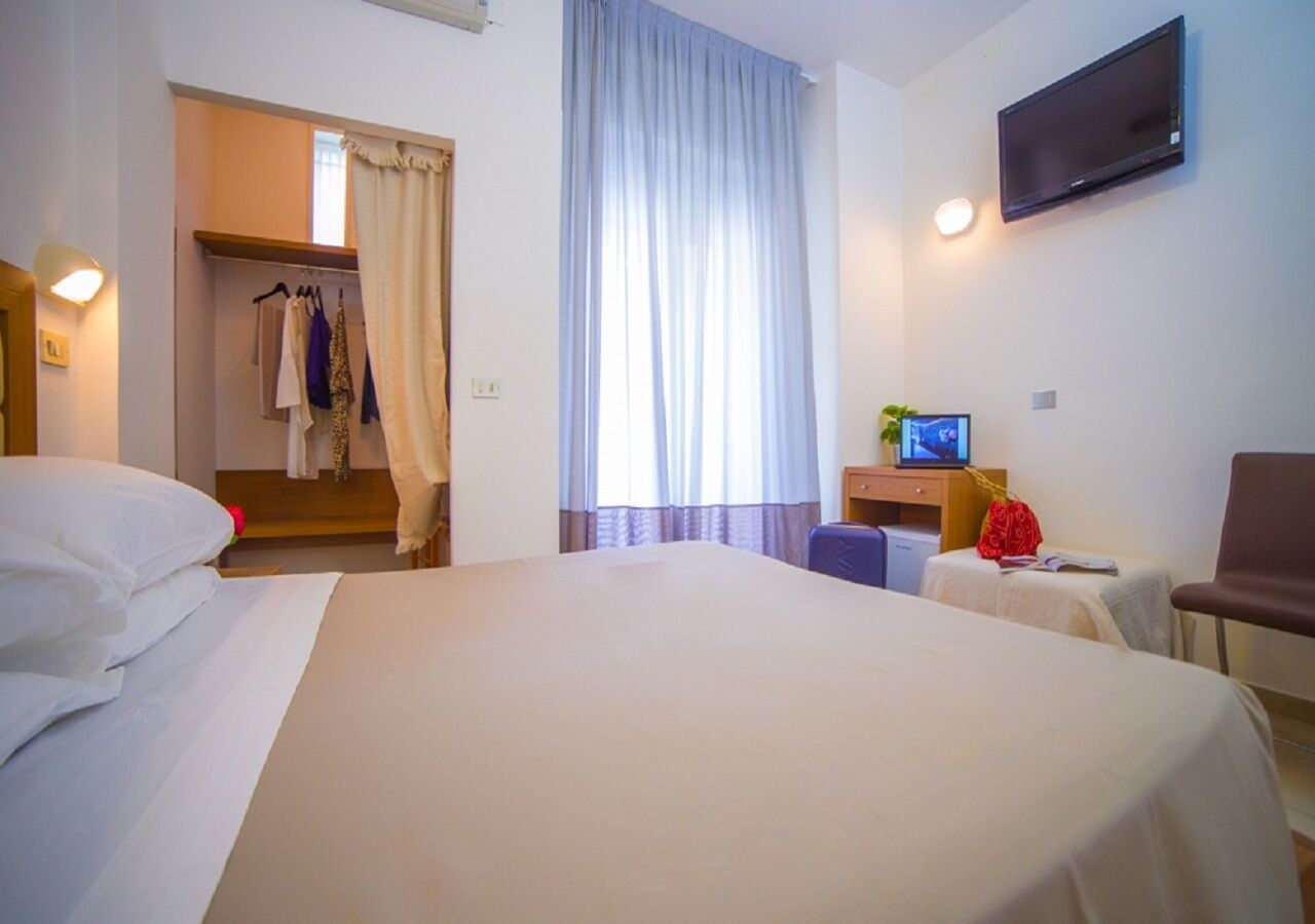 A hotel room with a large bed, a television, a desk with a computer, and a chair.