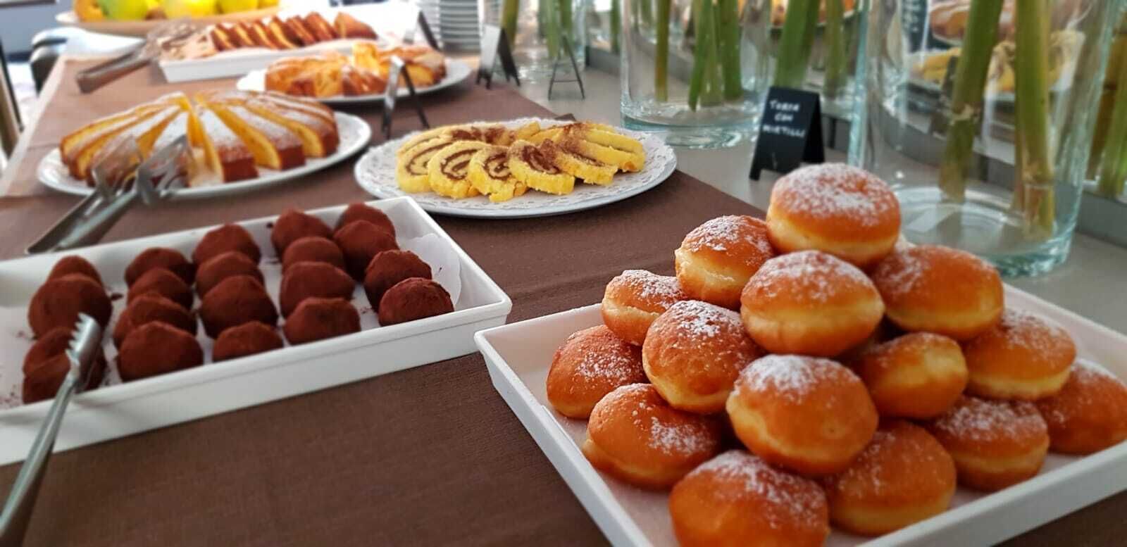 Een buffet met diverse gebakjes en desserts, waaronder rode velvet balletjes, kaneelbroodjes en suikerdonuts.