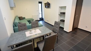 A modern living room with a grey sofa, a dining table with four chairs, and a TV mounted on the wall. - Quaint Holiday Home in Železná Ruda near Ski Area (Zelezna Ruda)