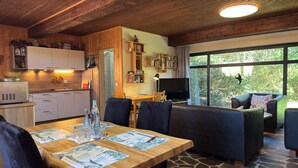 A cozy interior with a wooden ceiling, a dining area with placemats, a TV, and a view of greenery outside. - Grosses Ferienhaus Fuer 8 Personen, Manderscheid (Manderscheid)