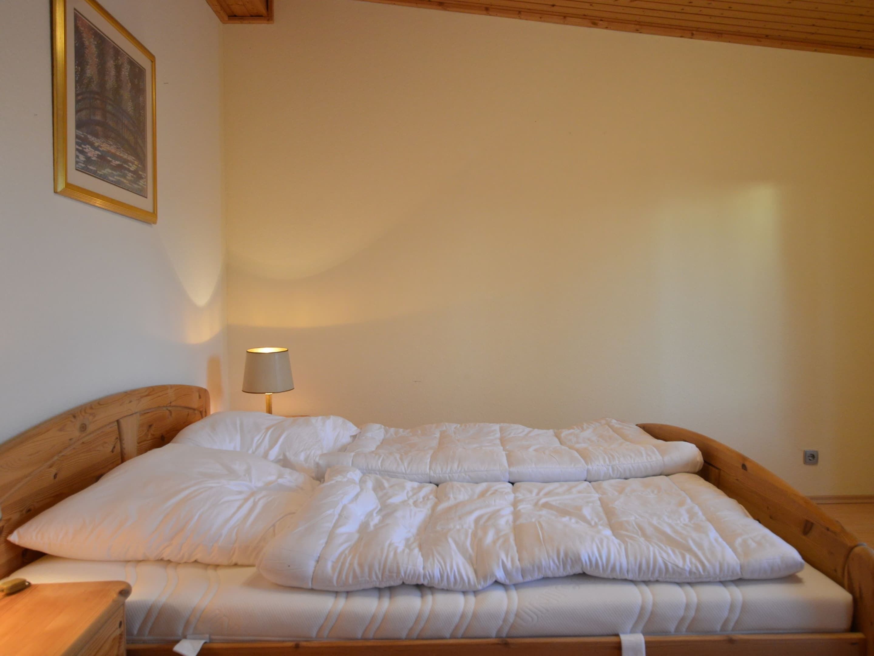 A wooden bed with white bedding in a room with a wooden ceiling and a framed picture on the wall.