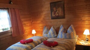 A wooden cabin bedroom with a bed, two bedside lamps, and a window with curtains. - Detached Wooden House with Fireplace & Large Garden near Bad Wildungen (Haina)
